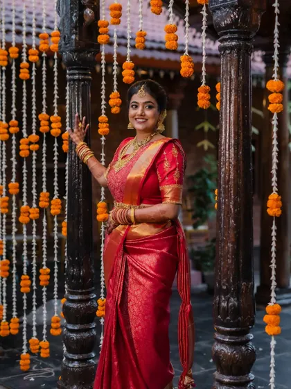 A portrait of the bride in her stunning red saree, framed by the rustic charm of her wedding venue. We focus on creating images that are both beautiful and full of character.