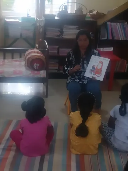 A storyteller shows the illustrations from a book about a special teatime guest. The children sit close, fully absorbed in the unfolding adventure.