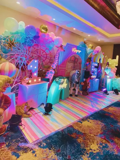 A vibrant, rainbow-colored carnival stage with clowns, a giraffe, and a lit-up number '1'.