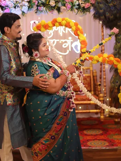 The couple performing a traditional ritual with a bow and arrow made of flowers, a key part of the Maharashtrian Dohale Jevan ceremony.