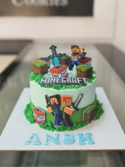 An action-packed Minecraft world built entirely from cake for a young gamer's birthday. This custom video game themed cake features edible characters, TNT blocks, and grassy terrain, all 100% eggless.