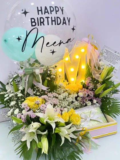 The full view of the personalized "Meena" birthday hamper, showcasing the vibrant floral arrangement, the custom balloon, and the light-up initial, all coming together to create a bright and cheerful birthday surprise.