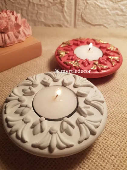 Two of our ornate Jesmonite T-light holders, with their flames lit. The design is inspired by traditional motifs, and they cast a beautiful, warm light perfect for Diwali or any celebration.