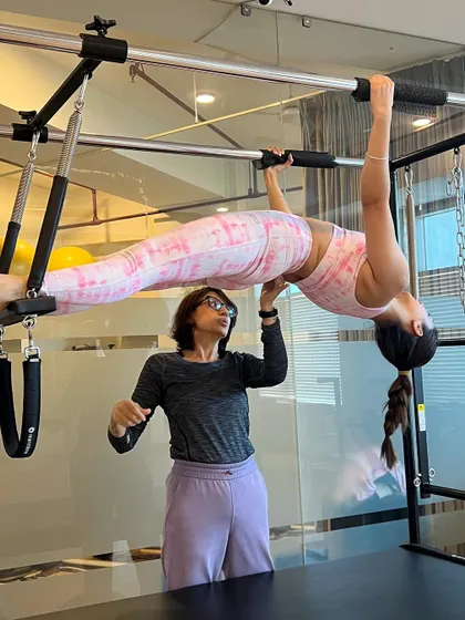 An instructor spots a client in a hanging pull-up on the Cadillac, an advanced move that builds incredible upper body and core strength.