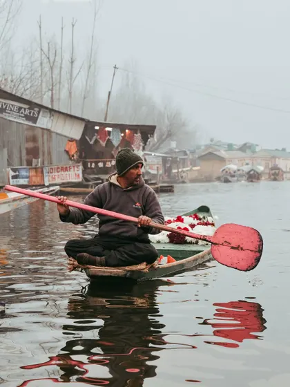 A flower seller on his boat in Kashmir, his bright red paddle reflected in the water. A slice of daily life on the lake.