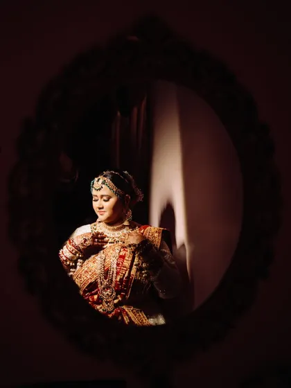 An artistic and moody mirror portrait. The bride is framed within the dark, ornate mirror, with a sliver of light illuminating her, creating a mysterious and captivating image.