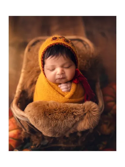 An autumn-inspired newborn photo with a cute pumpkin hat. The warm, earthy tones and cozy textures make for a beautiful and seasonal portrait of a peacefully sleeping baby.