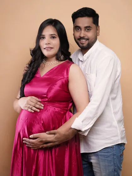 A classic studio portrait of an expecting couple. The simple tan background and their comfortable pose make for a warm and straightforward photo celebrating their pregnancy.