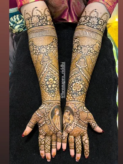 A classic bridal design featuring portraits of the bride and groom during the varmala ceremony. The palms are filled with intricate details, while the arms showcase traditional jhumka and bell motifs.