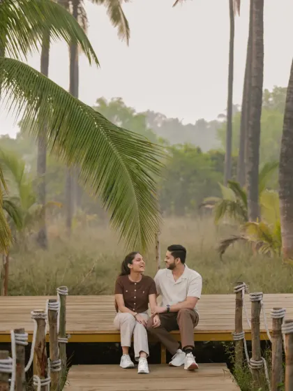 A lovely, composed shot of Vinay and Yachi sitting on a wooden deck. The framing with the large palm leaf adds a natural, tropical feel to this quiet, conversational moment.