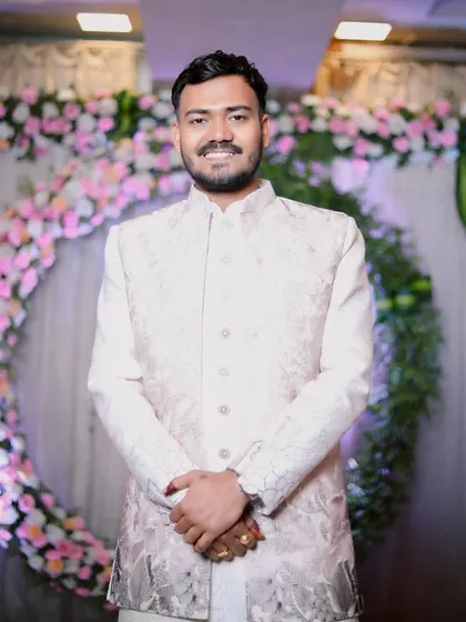 The groom stands proudly in front of a floral ring decoration at his engagement ceremony. His smile shows his excitement for the step he is about to take.