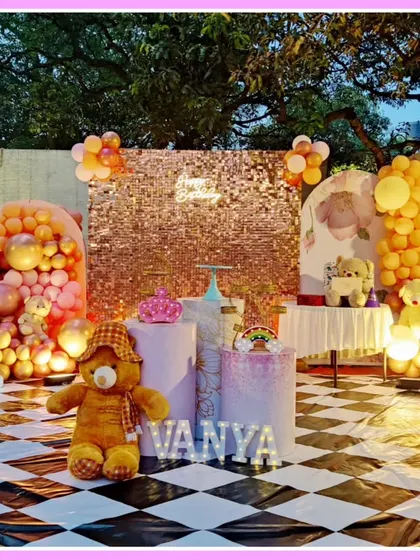 An outdoor teddy bear-themed first birthday. This setup features a checkered floor, a rose gold sequin wall, and adorable teddy bear props.