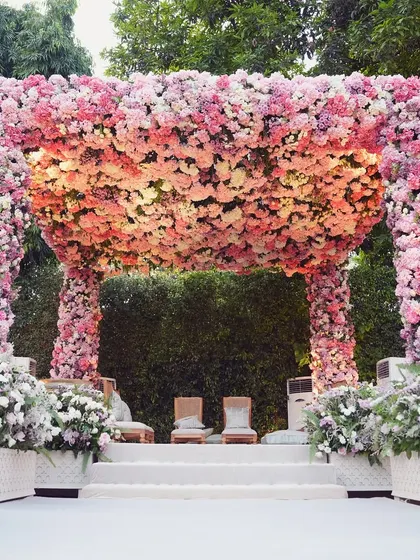 A breathtaking floral mandap designed for a romantic garden wedding ceremony. The structure is completely enveloped in thousands of fresh pink, peach, and ivory roses, creating a lush, fragrant, and unforgettable focal point for the couple's vows.