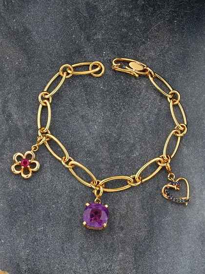 Charmed elegance. This stunning gold link bracelet is adorned with delicate charms: a ruby flower, a central amethyst, and a sapphire heart. It is perfect for adding a touch of personal luxury and colour to your everyday style.