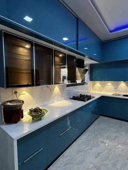A bold and glossy blue kitchen with a white marble-patterned countertop and backsplash. The under-cabinet and ceiling lighting make the high-gloss finish shine.