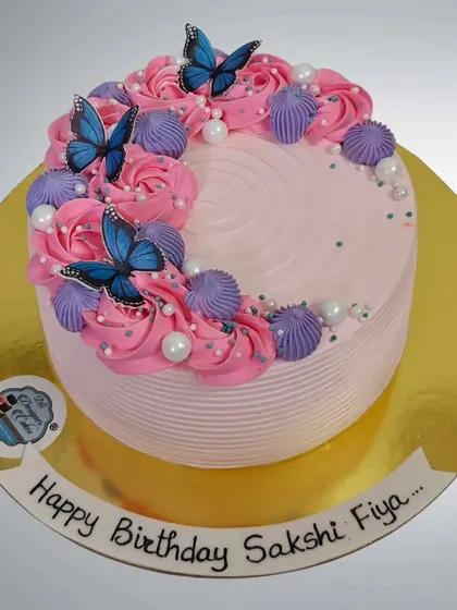 A pretty pink birthday cake decorated with blue butterflies and piped rosettes. The combination of colors creates a vibrant and cheerful design.