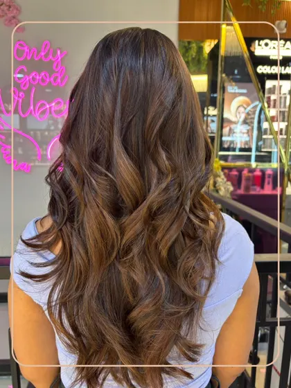 A gorgeous brunette balayage with soft, caramel tones. The "Only Good Vibes" neon sign in the background perfectly captures the feeling of a fresh new hairstyle.