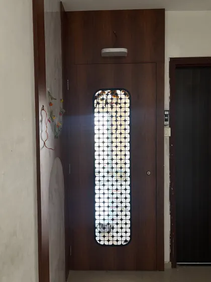 A dark wood safety door with a circular-patterned white jaali grill, offering a lovely contrast of colors and shapes.