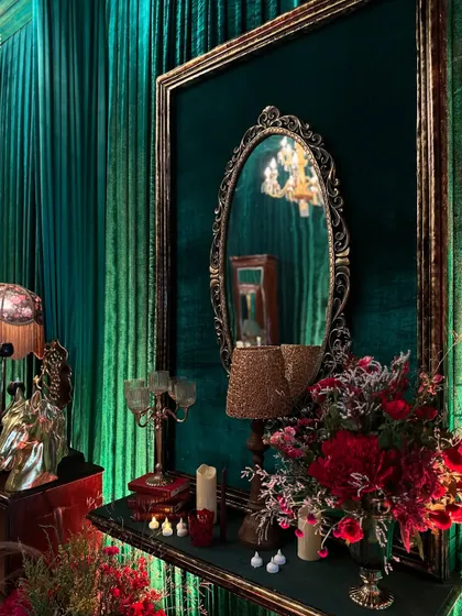 A captivating pathway decorated with vintage mirrors, red flowers, and elegant lamps against a backdrop of emerald green curtains, evoking timeless charm.