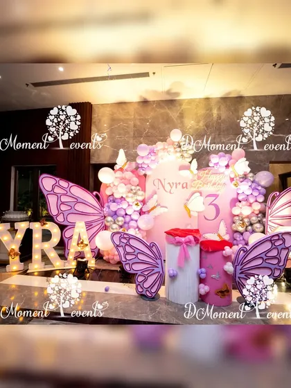 A stunning butterfly-themed stage in shades of pink and lavender, with large 3D butterfly wings and marquee letters creating a dreamy photo backdrop for a 3rd birthday.