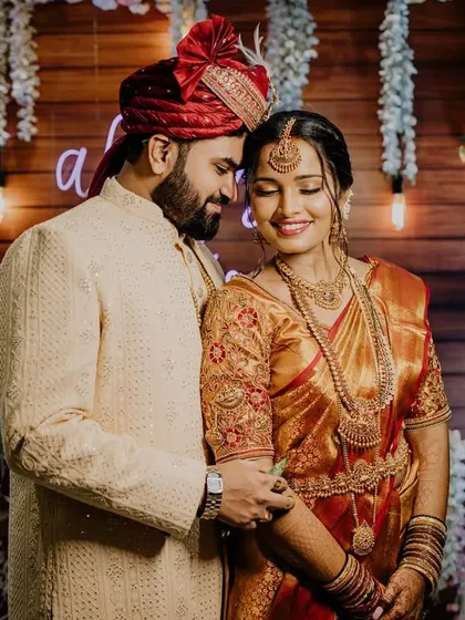 A classic portrait of a South Indian couple against a rustic, warmly lit backdrop. Their traditional attire and happy expressions make this a timeless wedding photograph.