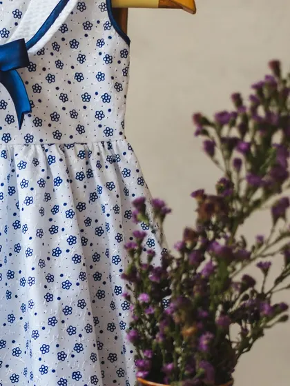 A simple yet charming white cotton dress with a blue floral print. The navy blue satin bow at the collar adds a classic, polished touch.