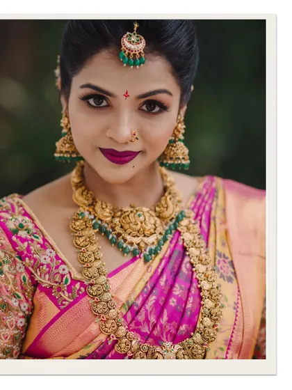 A close-up portrait of the bride, highlighting her striking makeup, intricate gold jewelry, and confident gaze.