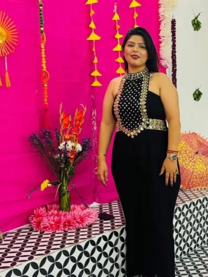 A full-length shot of the black embellished jumpsuit against a vibrant pink backdrop. The halter neck design is both elegant and glamorous.