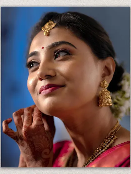 A radiant close-up of a bride, capturing her joyful expression and beautiful makeup. The focus on her traditional jhumkas and henna-adorned hand adds to the bridal charm.
