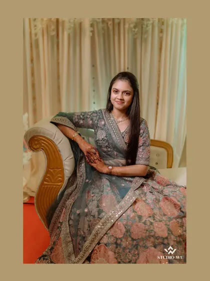 An elegant portrait of the bride seated, showcasing her beautiful floral lehenga. We focus on creating a relaxed and regal pose that highlights the intricate details of her attire.