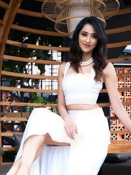 Radhika Narayan in a beautiful all-white outfit, seated in a unique wooden chair. The natural light and setting give this portrait a fresh and serene quality.