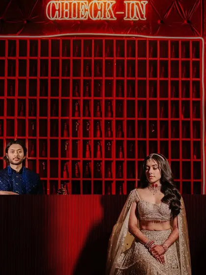 A moody and cinematic shot of the couple at a "Check-In" themed sangeet or cocktail night, creating a sense of story and intrigue.