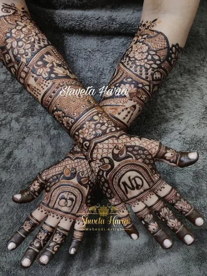 For your engagement, we can create a design that is both traditional and personal. This intricate mehendi features the couple's initials, 'ND', and interlocking rings, surrounded by classic peacock and floral motifs that extend up the forearm.