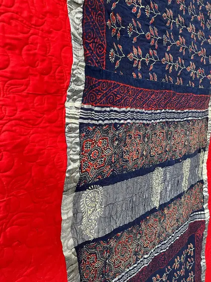 A close-up of the fabric and stitching on a reversible saree quilt, showing the rich textures and patterns.