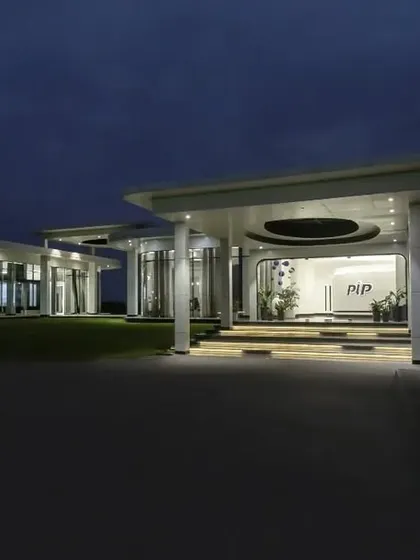 The same institutional building viewed at dusk, with interior lighting creating a warm glow. This highlights the building's transparency and showcases its structure against the evening sky.