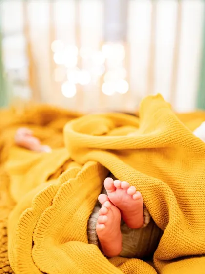 A close-up of tiny newborn feet peeking out from a warm blanket. A simple, beautiful detail captured in black and white.