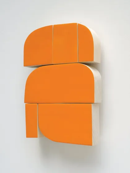 A vibrant orange abstract sculpture made of stacked, curved wooden blocks. This pop of citrus color adds a playful and modern touch to a minimalist wall.