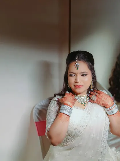 A quiet moment of the bride adjusting her jewelry while seated. This candid shot captures her elegance and the beautiful details of her white reception outfit.