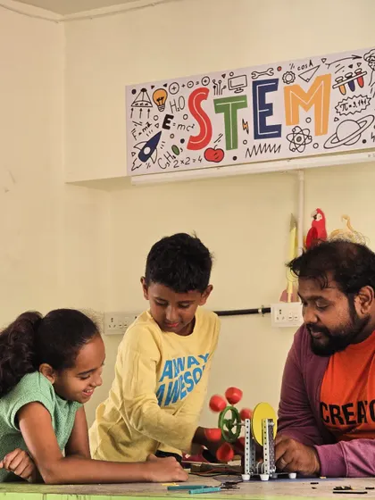 An instructor guides two students as they work on a mechanical model under our colorful "STEM" banner, showing our fun and engaging learning environment.