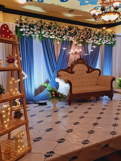 To personalize this reception stage, I added a wooden shelf with 'LOVE' marquee letters and other small decorative items. This adds a unique, personal touch to the main stage area, complementing the blue and white floral theme.