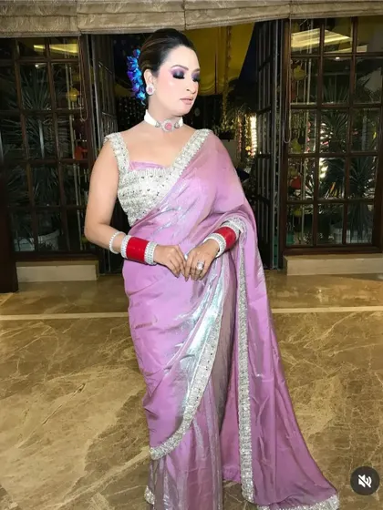 A full view of a client ready for a wedding event, showcasing a chic updo with a side-swept front. The hairstyle is designed to complement her saree and statement jewelry.