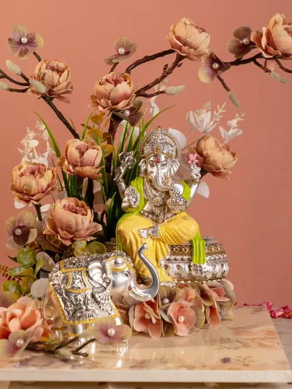 Blessings that bloom with beauty. This silver Ganesha idol, nestled among delicate flowers, creates a scene of divine tranquility. The accompanying silver elephant figurine adds a touch of prosperity and strength.