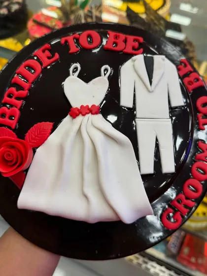 A classic "Bride to Be, Groom to Be" cake. The design features a fondant wedding dress and suit on a rich chocolate base, making it a perfect centerpiece for a pre-wedding celebration.