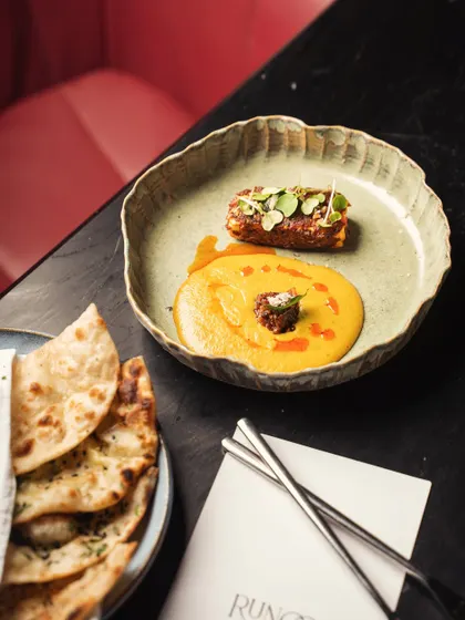 A deconstructed main course with naan bread, shot from above. The dark table and minimalist plating create a sophisticated and modern fine-dining look.