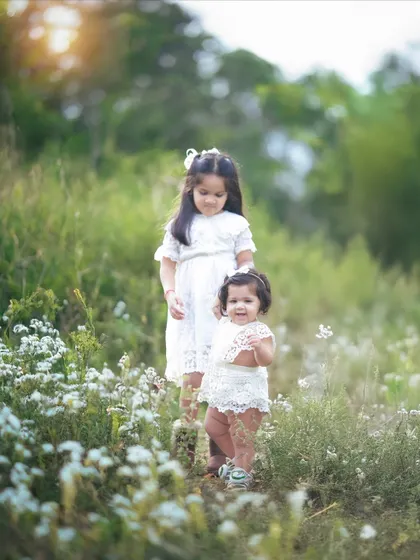 Two sisters standing together in a field of white flowers. The bond between them is so sweet and clear.