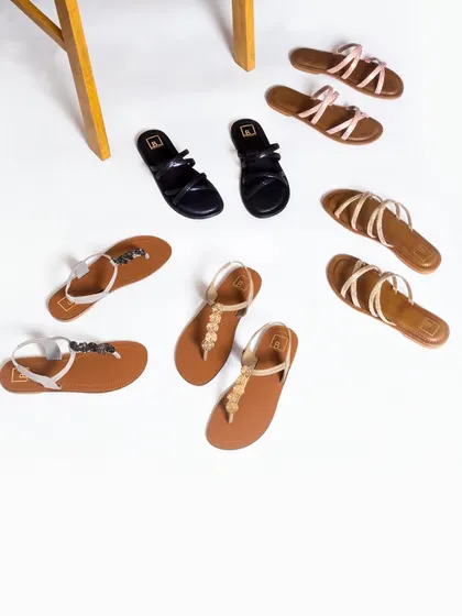 A creative flat lay of women's sandals on a clean white background, with a wooden stool adding a touch of lifestyle context.
