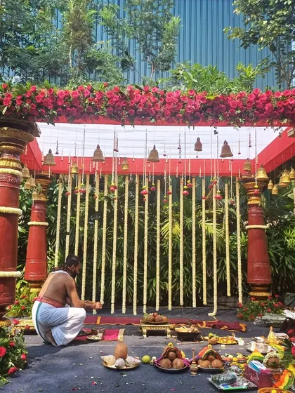 A classic South Indian mandap with red pillars, hanging temple bells, and a backdrop of tuberose strings.