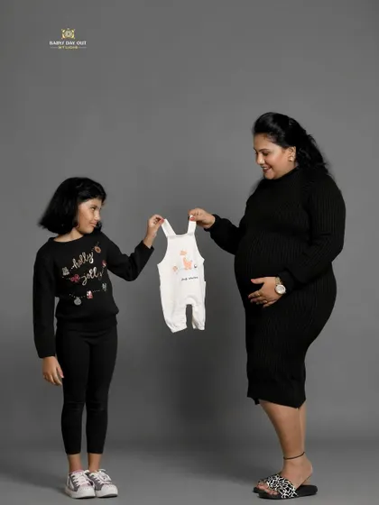 So much excitement for the new arrival. A mother and daughter hold up a tiny baby outfit, a simple and sweet pose that beautifully captures the anticipation of a growing family.