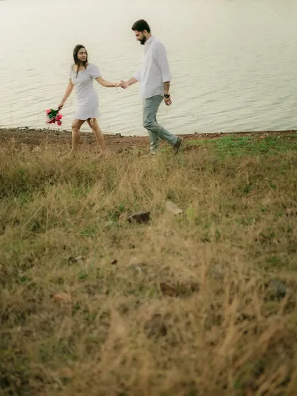 A couple walking through a grassy field by the water, a simple and romantic scene that tells a story of togetherness.