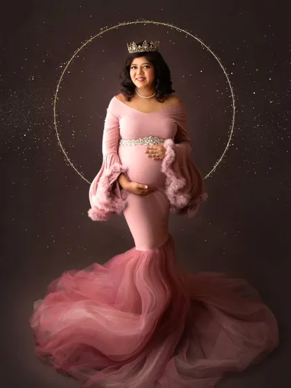 A truly magical fine-art portrait. This mom-to-be wears a stunning pink mermaid-style gown and a crown, framed by a halo of golden light.